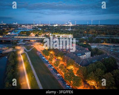 Vue aérienne du quartier de Veddel avec des bâtiments en brique, la ligne S-Bahn et la zone industrielle éclairée du port de Hambourg au crépuscule lors de l'heure bleue, Hamb Banque D'Images