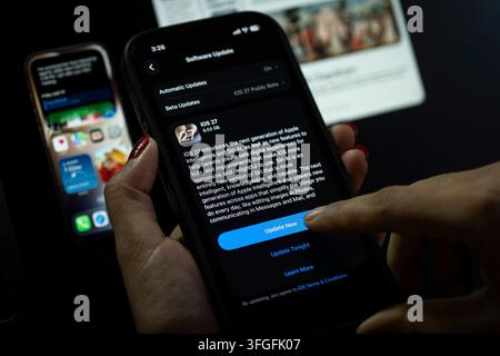 Dans cette illustration photo, une personne appuie sur le bouton „Mettre à jour maintenant“ sur un iPhone affichant l'écran de mise à jour logicielle iOS 27, mettant en avant la dernière nouveauté d'Apple Banque D'Images
