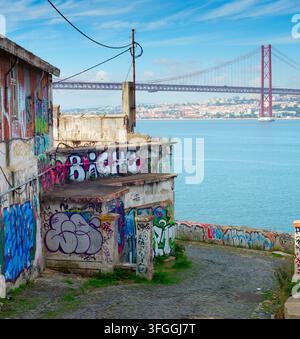 LISBONNE, PORTUGAL - nov 09, 2025 : vieux bâtiments couverts de graffitis vibrants se dressent près du front de mer à Almada, Portugal, avec le 25 avril Bridg Banque D'Images