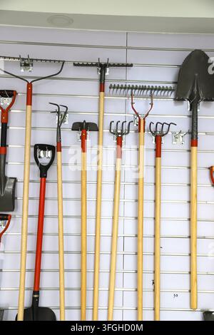 Devant un mur rayé blanc, un ensemble complet d'outils de jardinage est soigneusement exposé. Il comprend divers outils tels que des râteaux, des fourches et des pelles Banque D'Images