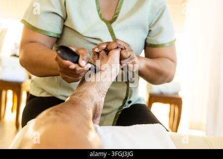 Vue en perspective en gros plan d'une masseuse utilisant un bâton de massage pour effectuer un massage traditionnel relaxant et thérapeutique des pieds et des jambes thaïlandais, en appuyant sur tous e Banque D'Images
