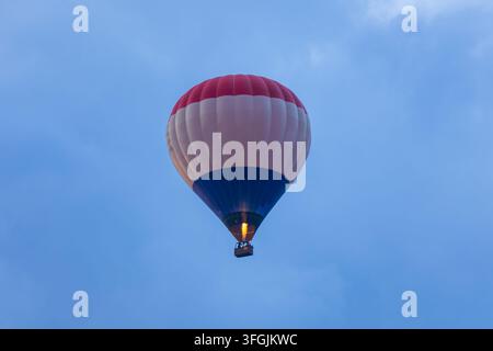 Un plan bas d'un ballon à air chaud rouge, blanc et bleu volant haut dans le ciel bleu Banque D'Images