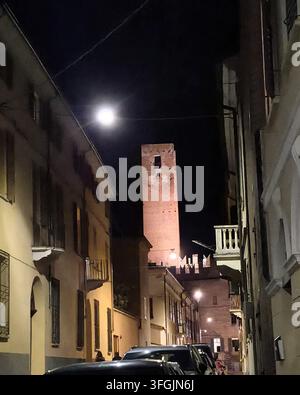 Une vue nocturne évocatrice le long d'une rue historique étroite montrant la Tour della Gabbia médiévale illuminée dans la vieille ville de Mantoue, en Italie. Banque D'Images