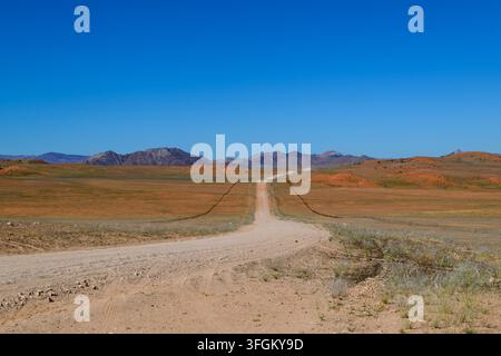 Paysage désertique vaste avec une route de gravier sinueuse menant vers des montagnes lointaines sous un ciel bleu clair. Le terrain est un mélange de plaines sablonneuses et de loess Banque D'Images