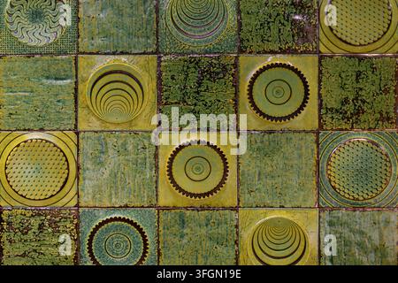 Carreaux de céramique verts texturés avec des motifs géométriques circulaires. Carreaux de céramique décoratifs verts et jaunes avec une glaze texturée et des cercles répétitifs Banque D'Images