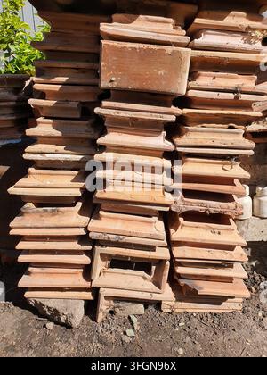 Une vue rapprochée de nombreuses tuiles en terre cuite usées empilées en rangées verticales contre un mur en béton brut. Les tuiles en terre cuite présentent des variations Banque D'Images