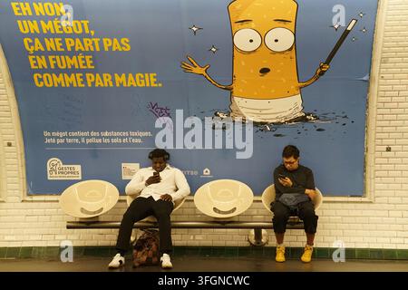 Deux hommes assis sur un banc du métro sous une affiche anti-cigarette sur un mur carrelé d'une station à Paris, France. Banque D'Images