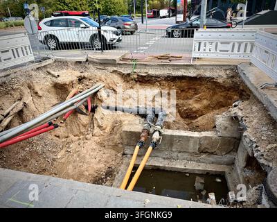 Vue grand angle d'un site de fouilles utilitaires souterrain avec des tuyaux exposés et une clôture de sécurité à une intersection urbaine. Banque D'Images