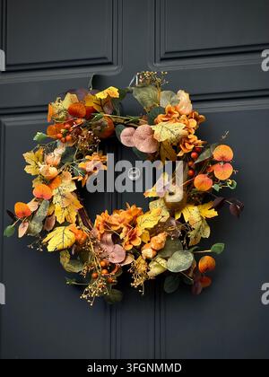 Gros plan vertical d'une couronne d'automne colorée avec des feuilles jaunes, des mini citrouilles et des baies orange accrochée à une porte à panneaux bleu marine foncé. Banque D'Images