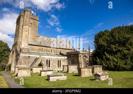 Église historique en pierre avec tour carrée et vieilles pierres tombales dans un cimetière ensoleillé sous un ciel bleu vif All Saints Church West Lavington Banque D'Images