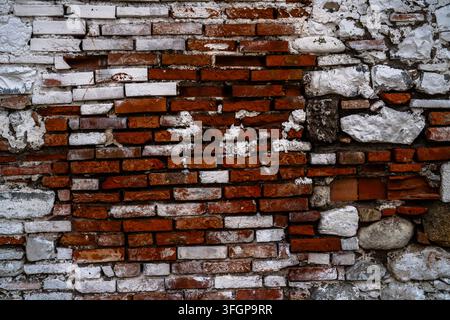 Surface détaillée d'un mur de maçonnerie vieilli combinant des briques rouges, des pierres pâles et du mortier, montrant une construction irrégulière, des phénomènes d'altération et des sections endommagées Banque D'Images