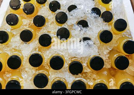 Bouteilles en plastique transparent non étiquetées de jus d'orange et de citron vert avec des bouchons noirs, refroidies dans de la glace pilée et prises de vue directement par-dessus Banque D'Images