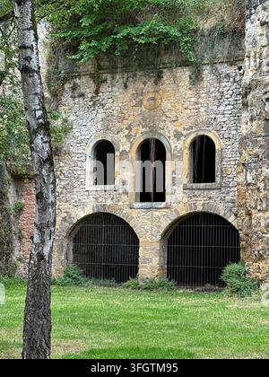 Ancien mur de forteresse en pierre avec des fenêtres en arcs et des entrées de tunnels grillagées. Mur de forteresse en pierre érodé présentant trois fenêtres supérieures en arcs sombres a Banque D'Images