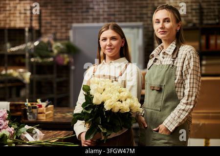 Portrait de deux fleuristes tenant un bouquet de roses dans une fleuristerie Banque D'Images