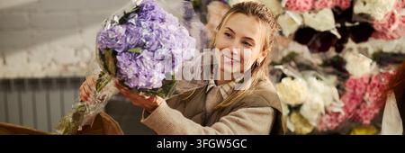 En-tête d'une fleuriste souriante tenant un bouquet d'hortensias dans une boutique de fleurs Banque D'Images