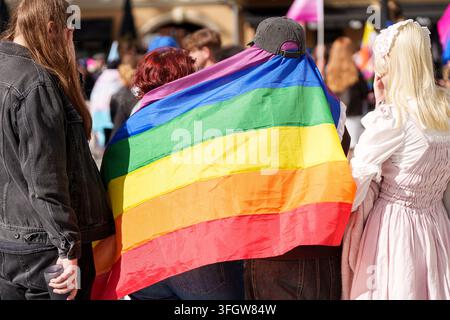 Person portant un drapeau arc-en-ciel de la fierté comme cape, entourée d'une foule lors d'un événement de parade de la fierté LGBTQ en plein air, concept de solidarité communautaire et de droits à l'égalité. H Banque D'Images