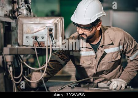 Homme indien utilisant un souffleur d'air pour le nettoyage de maintenance des déchets métalliques sur une table de fraisage dans l'industrie lourde du métal après le travail. Banque D'Images