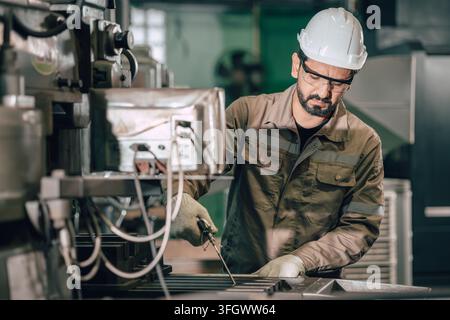 Homme indien utilisant un souffleur d'air pour le nettoyage de maintenance des déchets métalliques sur une table de fraisage dans l'industrie lourde du métal après le travail. Banque D'Images
