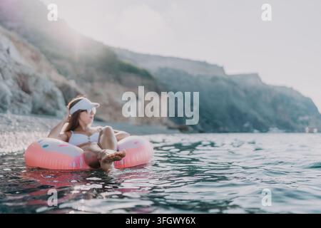 Femme, flottant, mer. Vacances d'été relaxantes sur un anneau gonflable près d'une côte rocheuse avec espace de copie ouvert. Banque D'Images