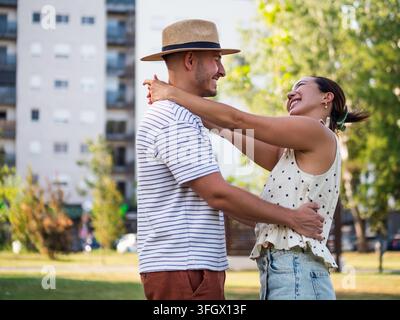 Jeune couple heureux s'embrassant et riant ensemble lors d'un moment romantique dans un parc ensoleillé. Banque D'Images