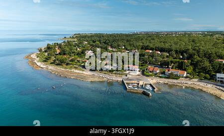 Village côtier paisible avec une petite marina, une côte rocheuse et une mer turquoise, entouré d'une forêt de pins dense et de maisons éparses de style méditerranéen Banque D'Images