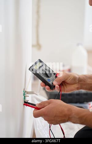 Électricien testant une prise murale avec un multimètre numérique. Homme vérifiant la tension et la puissance avant les travaux électriques. Électricité, câblage et électrique Banque D'Images