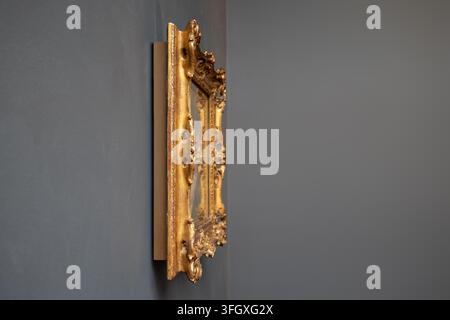 Cadre de tableau antique en or orné, mettant en valeur des détails baroques complexes et un artisanat, accroché à un mur gris foncé dans une galerie Banque D'Images