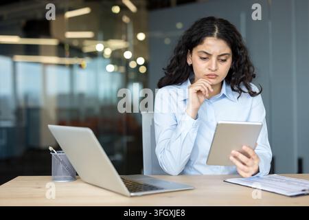 Femme d'affaires concentrée utilisant une tablette pour une analyse financière au bureau avec un ordinateur portable dans un environnement de bureau d'entreprise. Gestionnaire professionnelle travaillant sur des documents de stratégie et de planification dans un environnement de travail moderne. Banque D'Images