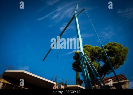 Flèche et tour d'une grue de construction bleue contre un ciel bleu clair et un pin. Banque D'Images