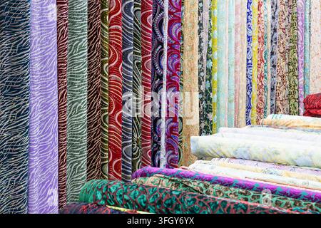 Bobines de tissu colorées suspendues dans une boutique de textiles sur un bazar oriental à Boukhara, Ouzbékistan. Motifs vibrants et textures riches idéales pour les voyages, cul Banque D'Images