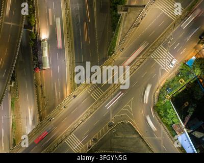 Vue aérienne d'un échangeur autoroutier la nuit avec des traînées de lumière des véhicules en mouvement et l'infrastructure urbaine à Pune, Maharashtra, Inde. Banque D'Images