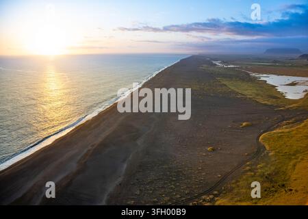 Admirez le coucher de soleil époustouflant illuminant les falaises de Dyrholaey et la plage de Vik. Le littoral de sable noir s'étend le long de l'Atlantique, créant un Banque D'Images