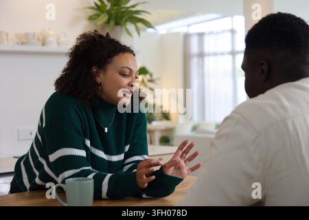 Amis afro-américains discutant à table à la maison, femme penchée en gesticulant tenant un pendentif en forme de mug vert Banque D'Images