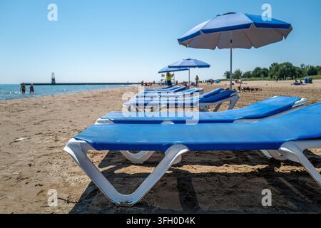 Chaises longues bleues vides et parasols alignés le long du rivage sablonneux de Kathy Osterman Beach sur le lac Michigan, regardant vers la jetée Banque D'Images