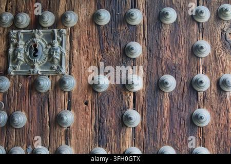 Serrure ornée et porte en bois cloutée – Une vue rapprochée d'une porte en bois antique présentant une serrure en métal ornée de visages sculptés et de nombreuses décorations Banque D'Images