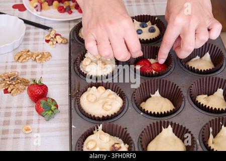 Mains décorant des muffins maison avec des baies fraîches et des noix Banque D'Images