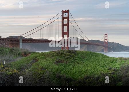 Capturé depuis une colline luxuriante, cette vue tranquille met en valeur le pont emblématique du Golden Gate de San Francisco qui enjambe la baie sereine en contrebas. Banque D'Images