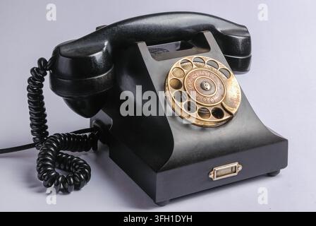 Téléphone à cadran rotatif noir vintage avec câble spiralé sur fond blanc Banque D'Images