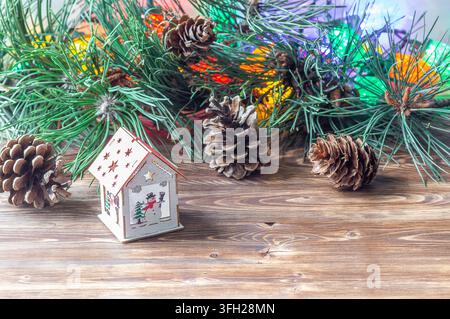Petite maison en jouet en bois avec un motif de bonhomme de neige sur une table en bois avec des branches et des cônes de pin. Banque D'Images