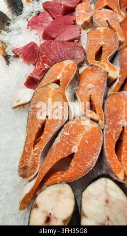 Tranches de filets de thon rouge frais et steaks de saumon orange vif disposés sur un lit de glace pilée, mettant en avant des choix sains pour les fruits de mer et la cuisine Banque D'Images
