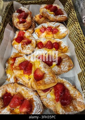 Des pâtisseries danoises aux fraises et crème fraîchement cuites remplissant un panier en osier, saupoudrées de sucre glace, offrant une délicieuse gourmandise pour le petit-déjeuner ou en dessert Banque D'Images