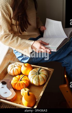Adolescente lisant un livre près de la fenêtre avec des citrouilles à la lumière d'automne Banque D'Images