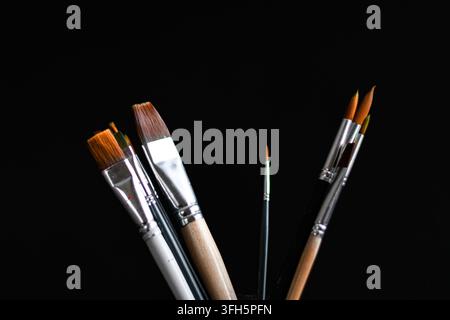 Assortiment de pinceaux d'artiste de formes et de tailles différentes disposés dans un récipient sur un fond noir foncé. Banque D'Images