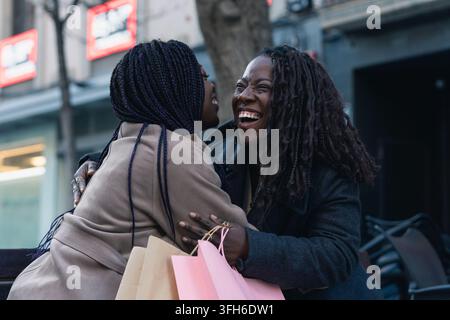 Des amis africains heureux s'étreignent après une session de shopping en ville Banque D'Images
