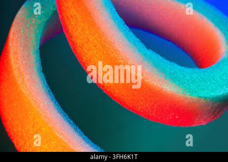 Vue macro en gros plan d'anneaux de mousse entrelacés brillant dans des tons vifs de néon orange, rouge, turquoise et bleu, créant un fond abstrait texturé doux Banque D'Images