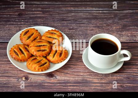 Plusieurs mini tartes à la confiture de pommes dans une assiette ronde et une tasse de café noir sur une table en bois. Vue de dessus, flat lay. Banque D'Images