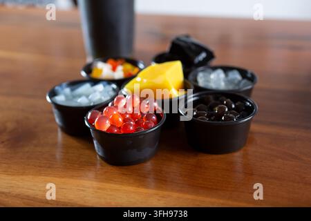 Une vue d'une variété de toppings et d'ingrédients populaires pour le thé au lait, dans des coupelles à condiments en plastique noir. Banque D'Images