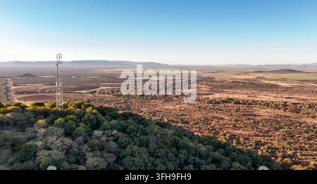 Vue aérienne d'une tour de télécommunications dressée sur une colline boisée surplombant un vaste paysage rural avec des champs agricoles et des buissons arides à Ru Banque D'Images