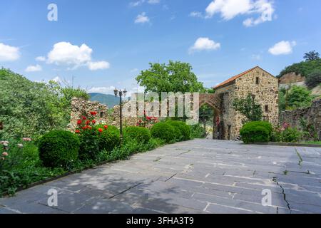 Mur de pierre et passage vers l'église de la Sainte-Trinité près de la ville de Kazreti. Murs en pierre claire, un beau jardin avec des arbres et des fleurs Banque D'Images