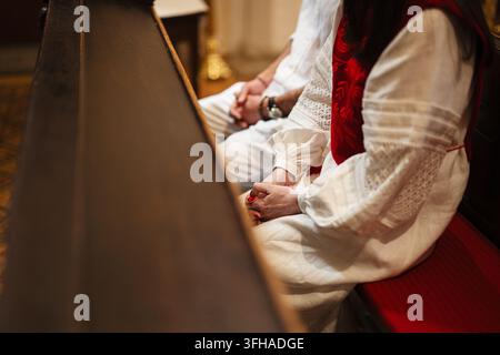Couple assis côte à côte sur un banc d'église, les mains jointes dans un moment calme de prière et de dévotion. Banque D'Images